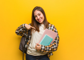 Young student woman person pointing by hand to a shirt copy space, proud and confident