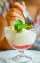 young girl's hand holding a spoon and eating ice cream in glass at a table in cafe