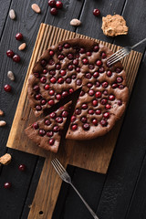 Homemade comfort food. Flatlay of chocolate pie with tart cherries with cocoa beans and cane sugar on dark background