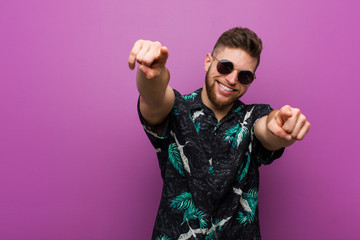 Young man wearing a vacation look cheerful smiles pointing to front.