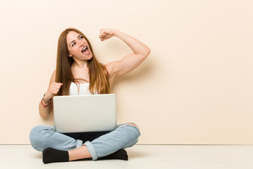 Young ginger woman sitting on her house floor raising fist after a victory, winner concept.