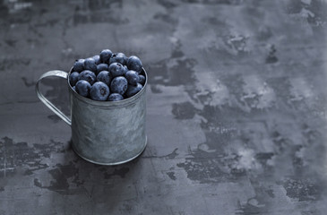 Fresh blueberry berries in an iron mug on a dark background. Copy space