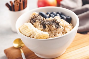 Oatmeal porridge with blueberries, banana and chia seeds in bowl. Closeup view, selective focus, toned image. Healthy breakfast food. Concept of clean eating