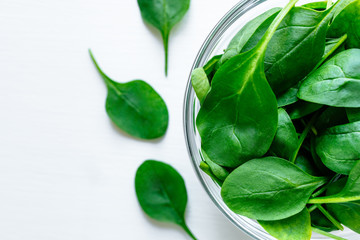 Fresh green spinach leaves in glass bowl on white table. Organic food, healthy diet, vegetarian food. Top view.