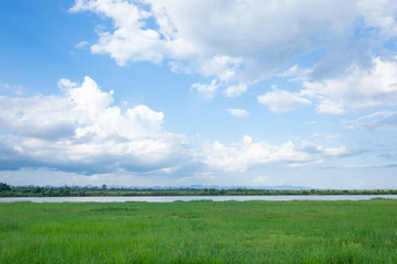 Green field, river and blue sky with light clouds backgrund