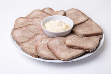 Beef boiled tongue with horseradish on a white plate. White background, isolated. Close-up.