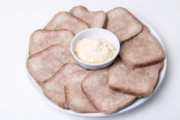 Beef boiled tongue with horseradish on a white plate. White background, isolated. Close-up.