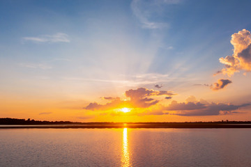 Sunset reflection lagoon. beautiful sunset behind the clouds and blue sky above the over lagoon landscape background. dramatic sky with cloud at sunset © Achira22