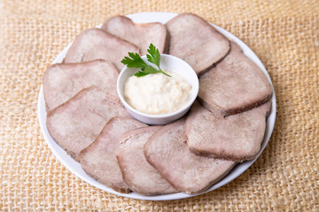 Beef boiled tongue with horseradish on a white plate. Close-up.