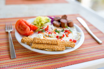 Plate with fried eggs, sausages, tomatoes, paprika and toasted sticks with sesame