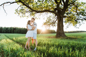 Young pretty couple in love standing in park. Handsome cheerful blonde girl in white dress hugging her boyfriend. Man and woman having fun outdoors