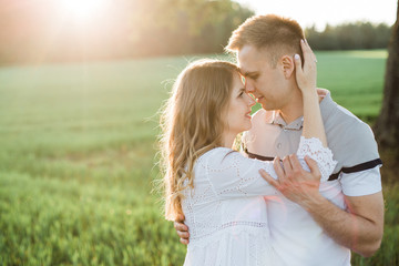 Obraz premium Young pretty couple in love standing in park. Handsome cheerful blonde girl in white dress hugging her boyfriend. Man and woman having fun outdoors