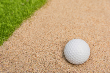 White golf ball in sand bunker on golf court.