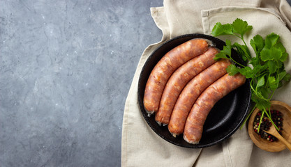 Raw uncooked meat sausages, herbs and spices in a black iron pan. Top view with copy space. Gray concrete background.