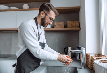 young man washing tomatoes under the tap in the kitchen
