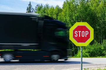 red stop road sign in the foreground and blurred fast truck in the background