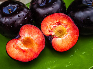 Three dark purple plum fruits and one cut close-up