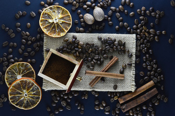 Fototapeta na wymiar Fresh natural coffee beans scattered on a dark blue background with cinnamon sticks, sliced ​​orange slices