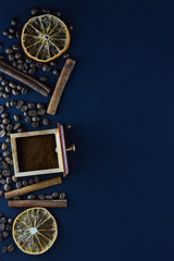 Fresh natural coffee beans scattered on a dark blue background with cinnamon sticks, sliced ​​orange slices