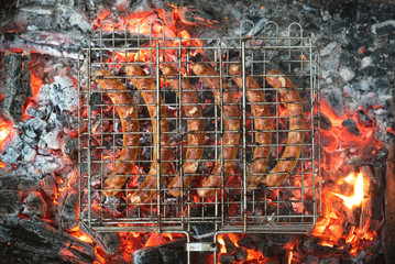 A grilled sausages on a metal grate above a burning coals background.