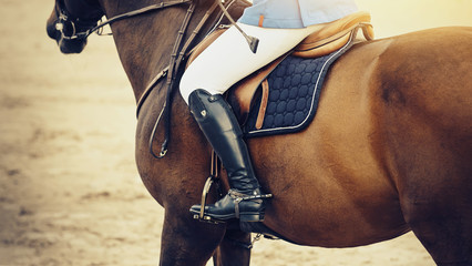 Equestrian sport. The leg of the rider in the stirrup, riding on a red horse.