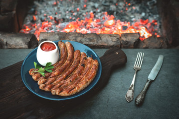 A grilled sausages on a plate on a kitchen table with a burning coals background.