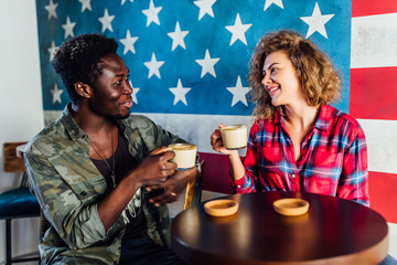Cheerful male and female teen best friends sitting on cafe terrace drinking coffee and speaking.