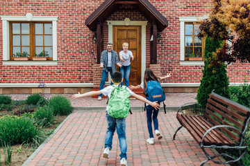 Photo of the back. Two small children  after school  cooming to grandparents ,with schoolbag on shoulders. Happy meeting.