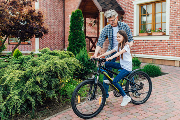 Handsome, cute  grandather teach his granddaughter to ride a bike. Together better.