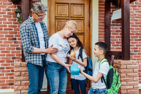 Grandparents  seeing daughter  and son off to school standing on the porch of the house, sends her a snack. Bright morning street. Lovely concept.