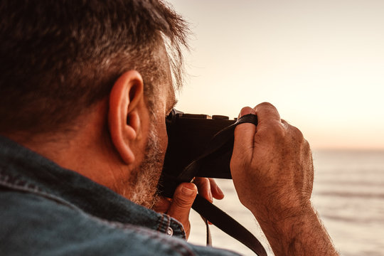 Mann im seitlichen Profil  mit Kamera in der Hand fotografiert das Meer 