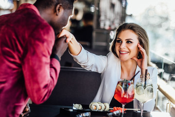 Man is kissing hand of his pretty woman. Romantic couple in cafe is drinking mojito with sushi.