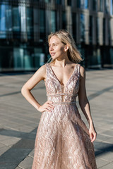 Beautiful blonde girl posing in a long beige dress on the background of a modern building.