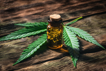 Cannabis essential oil in the vial with a green leaf on a wooden board background. Herbal medicine...