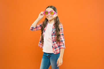 Eyeglasses perfect for her style. Little child looking happy in fashion eyeglasses. Small kid smiling with party eyeglasses on orange background. Funny girl wearing sun eyeglasses with color filter