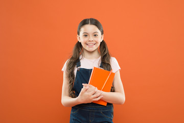 favorite book. happy little girl with notebook. reading book. literature lesson. back to school. school girl on orange background. kid diary. writing notes. poetry and novel. modern education