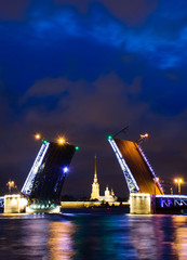 Fototapeta na wymiar A drawbridge of Saint Petersburg at night with a fortress between it and lights reflected in water. Dvortsoviy bridge and the Neva river. White nights. Famous sight in the city of Russia