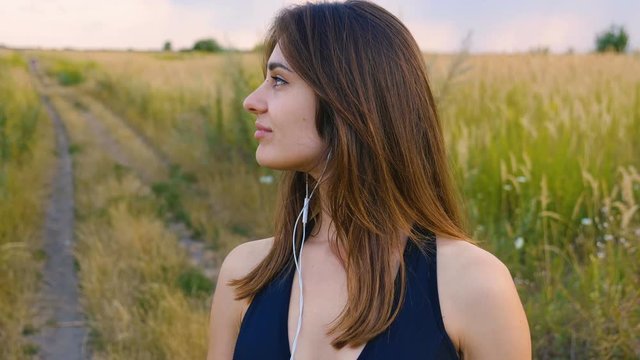 Happy young woman use smartphone and headphone standing in field at sunset, healthy lifestyle. Sportywoman runner using smartphone outdoor.