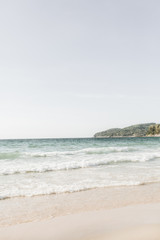 Schöner tropischer Strandblick mit weißem Sand, blauem Meer mit Wellen und grüner Insel am Horizont auf Phuket, Thailand. Minimale Komposition mit neutralen Farben. Sommerkonzept. Natürlicher Hintergrund.