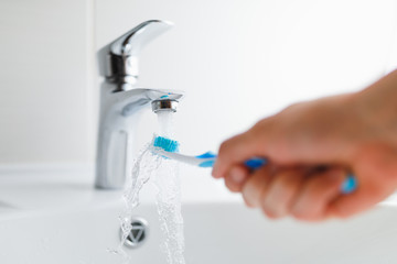 hand holding toothbrush under flowing water from faucet