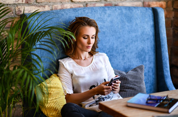 Pretty young girl resting on a big soft blue chair in a cafe or at home, chatting on the phone, chatting time.
