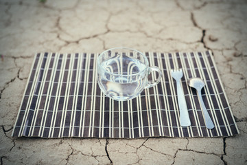 Water is the most necessary food for a person. A cup of water and cutlery on the dried ground.