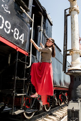 A woman in a red dress and a cap with a star stands on the bandwagon of the old Soviet locomotive.
