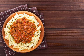 Homemade vegan bolognese sauce made with soy meat, fresh tomatoes, onion and garlic served on fusilli pasta on wooden plate, photographed overhead with copy space on the right side