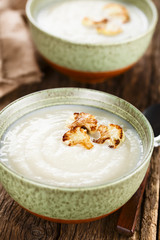 Fresh homemade cream of cauliflower soup garnished with roasted cauliflower floret slices (Selective Focus, Focus on the front of the right floret on the first soup)