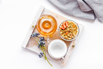 Breakfast in bed with granola, tea and fruit on tray on white background top view