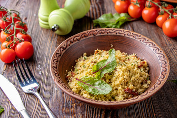 Couscous in bowl with olive oil and dried tomatoes on wooden background, oriental cuisine, horizontal photo