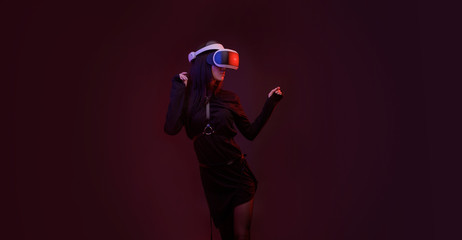 Obraz premium Beautiful woman in fashion dress posing over dark background. Gamer girl in glasses of virtual reality. Augmented reality, game, hobby concept. VR.