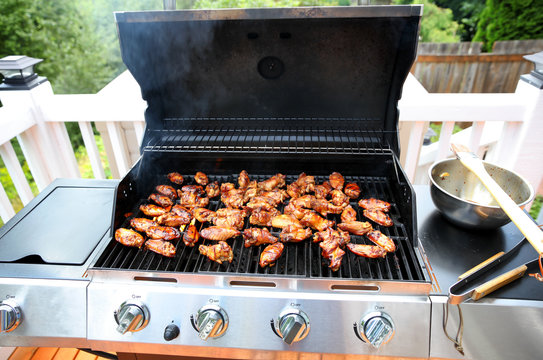 Open barbecue grill cooking chicken wings on outdoor deck during summer season