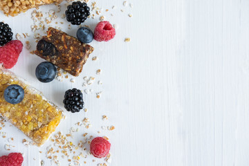 Frame for text with granola and natural berries of raspberry, blackberry, blueberry and oatmeal on a white wooden background. Useful cereal bars for snacking and breakfast